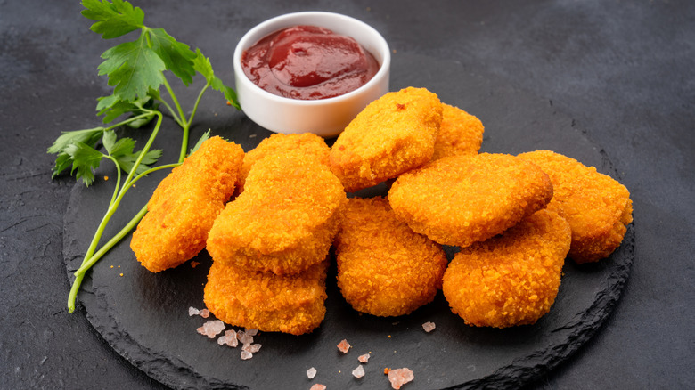 chicken nuggets on a black plate with a cup of ketchup
