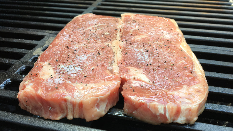 Two raw New York strip steaks on the grill