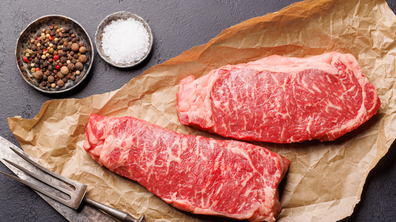 Sirloin steak on brown paper with a small bowls of salt and pepper on a table