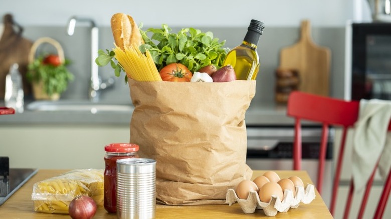 a paper bag filled with groceries sits on a wooden table in a kitchen