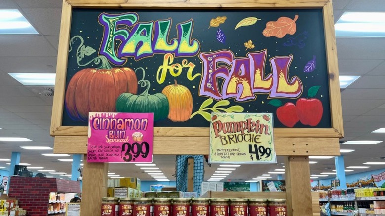 Sign in Trader Joe's with colorful lettering saying "fall for fall" with pumpkin drawings above shelf of spreads