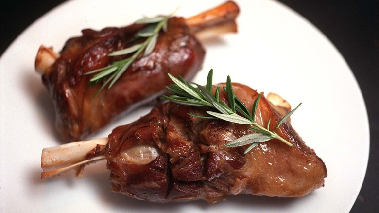 Two roasted lamb shanks topped with rosemary on a white plate