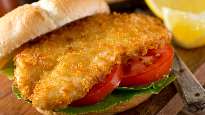 A homemade fish sandwich on a bun with lettuce and tomatoes on it.