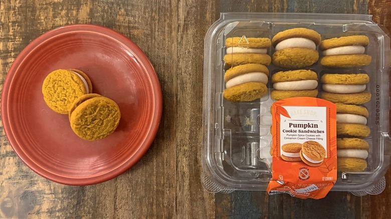 Bake shop Pumpkin sandwich cookies from Aldi in clamshell package next to plate of two cookie sandwiches
