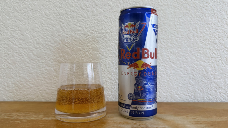 Red Bull can beside a small, half-full glass