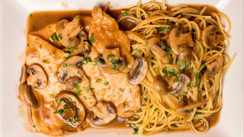 Chicken marsala on a rectangular plate with spaghetti
