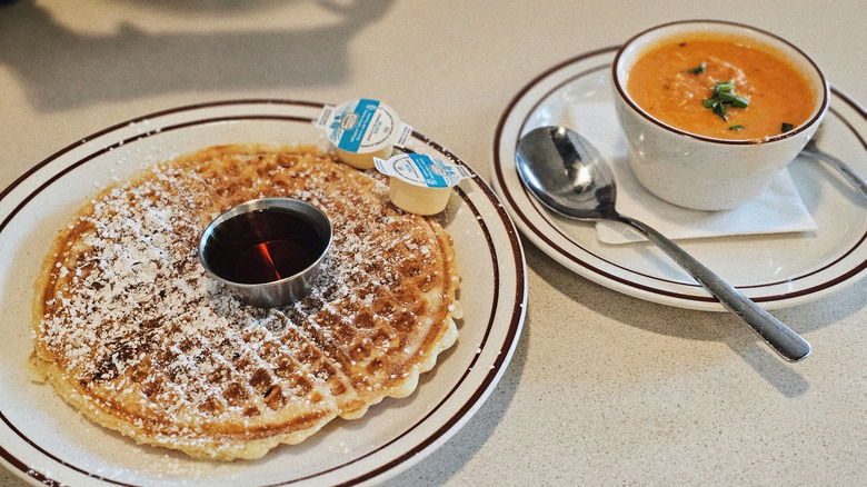 Waffle with powdered sugar on a white plate and soup in a white bowl at Waffle House