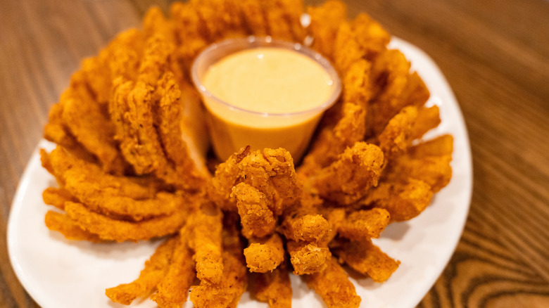 A Bloomin' Onion on a white plate with dipping sauce in a cup in the middle.