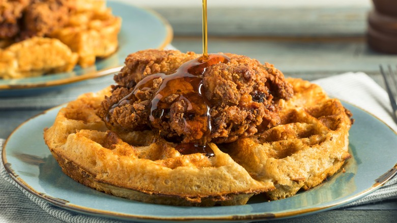 A plate of freshly served chicken and waffles with syrup drizzling on top