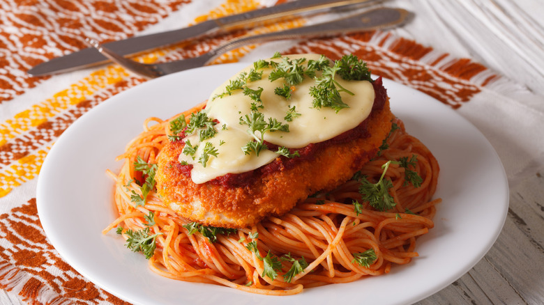 Chicken parmesan garnished with herbs served over spaghetti in a while dish