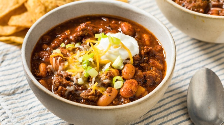 A bowl of chili topped with cheese, sour cream, and pickled jalapeno.