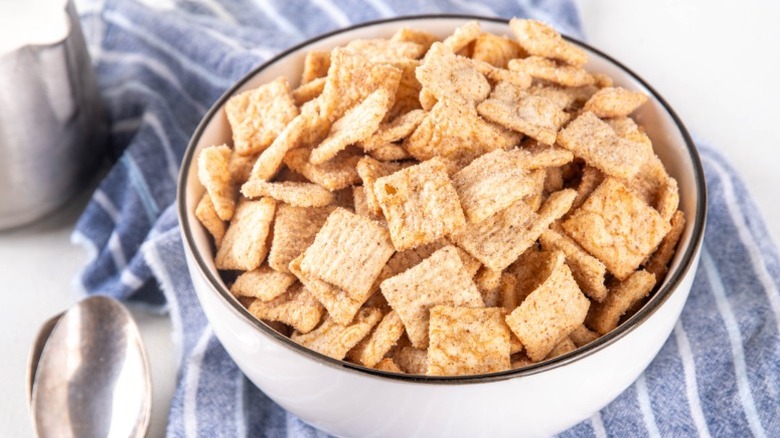 A full bowl of Cinnamon Toast Crunch with a spoon next to it on a table.