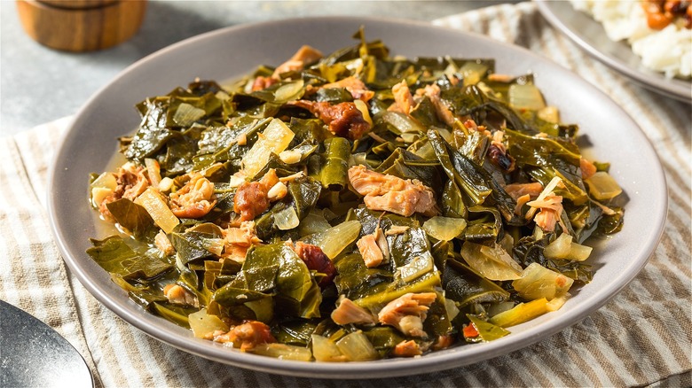 Cooked collard greens and pork on a gray plate over a cream-and-tan-striped dishcloth
