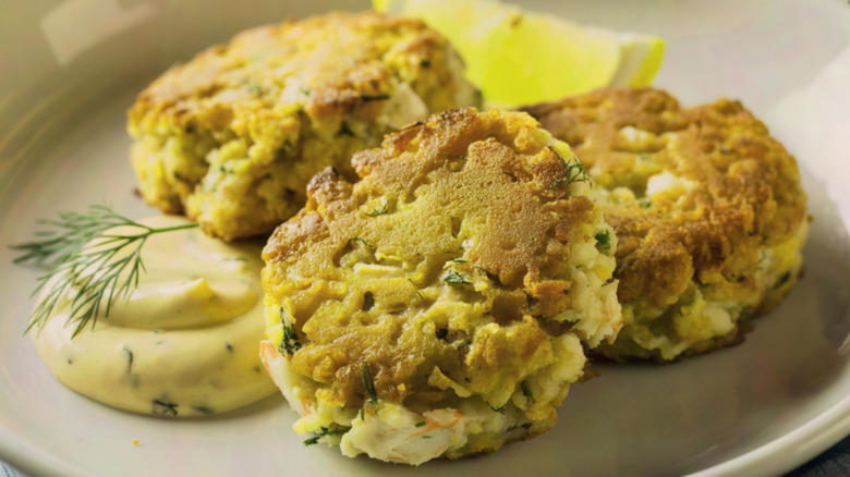 crab cakes on a white plate with a lemon wedge, a dill frond, and some remoulade sauce