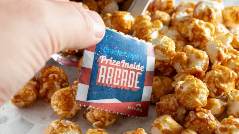 A hand pulling a prize out of a bag of open Cracker Jack snack mix.