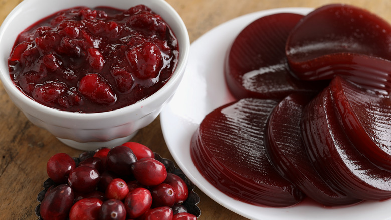 Bowl of cranberry sauce next to a plate of slices of canned cranberry sauce and cranberries