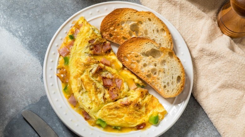 A classic Denver omelet served on a white plate with two pieces of toast.