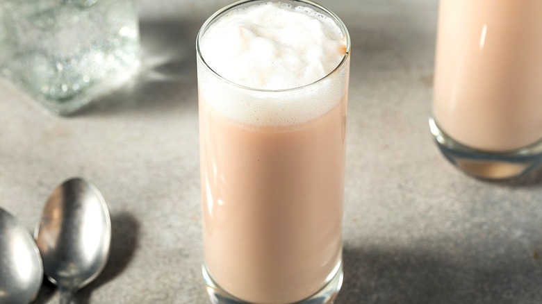 Egg cream beverage in a tall clear glass next to two silver spoons