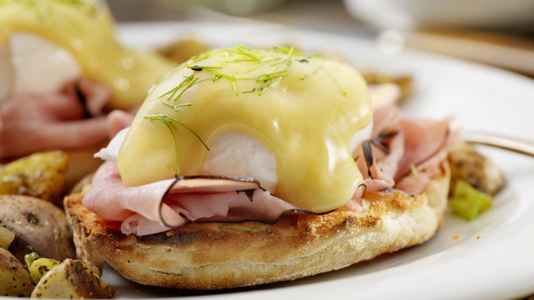 eggs benedict on a white plate with fried potatoes
