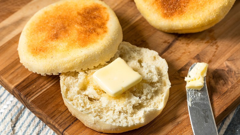 An English muffin sliced in half with butter on a wooden serving board