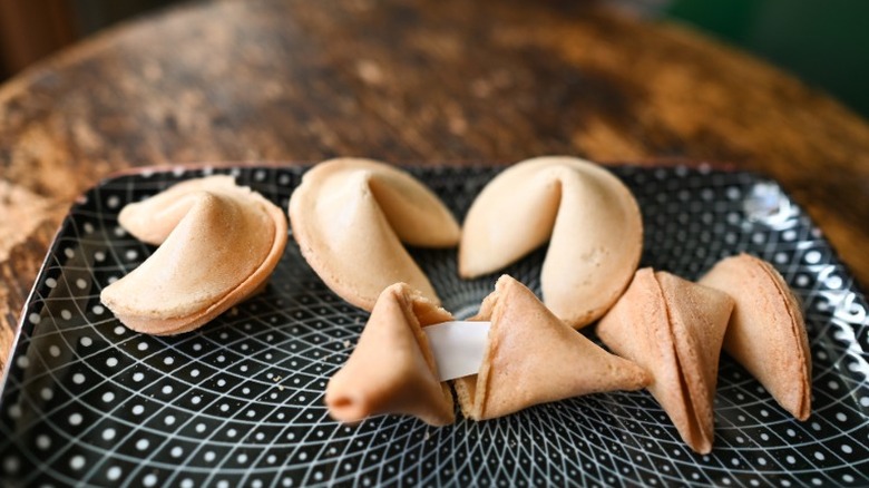 Fortune cookies sitting out on a tray with one cracked open with a paper message showing.