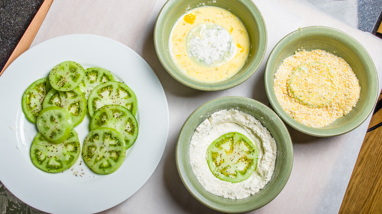 Preparing fried green tomatoes with green bowls of ingredients