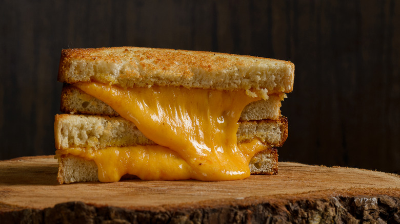 Melted cheddar oozing out of a grilled cheese sandwich on a wood block