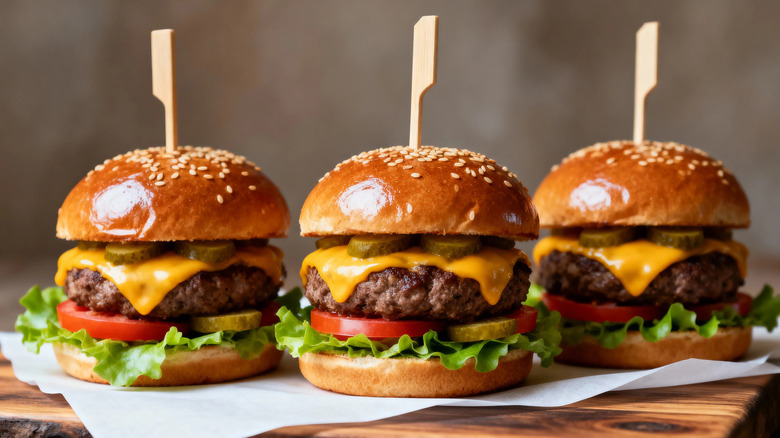 Three cheeseburgers sitting on a wooden cutting board