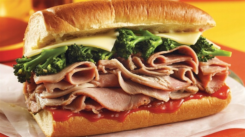 A roast pork sandwich with provolone cheese, sauce, and broccoli rabe on Italian bread.