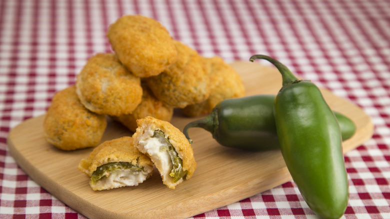 Jalapño poppers and two whole jalapeños on wooden cutting board.