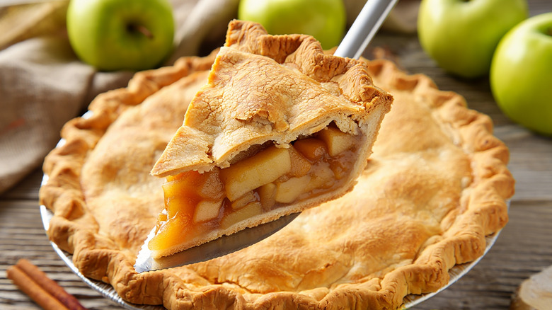 cutting out a slice apple pie with granny smith apples in the background