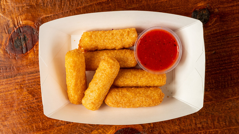 Mozzarella sticks sit with a container of marinara sauce in a paper boat