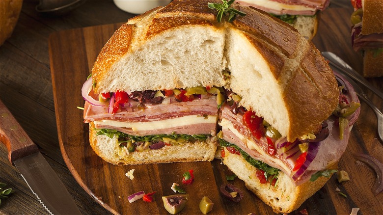 Cut muffuletta sandwich layered with cold cuts, provolone cheese, and olive salad on a wooden serving board