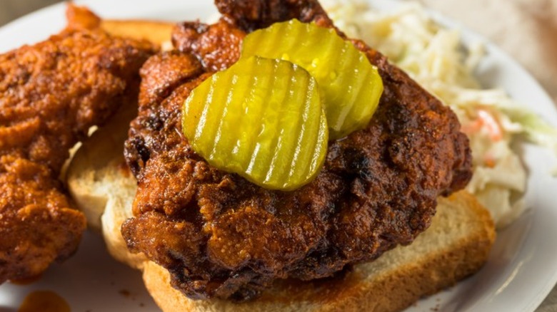 Nashville hot chicken on a plate with pickles and bread.