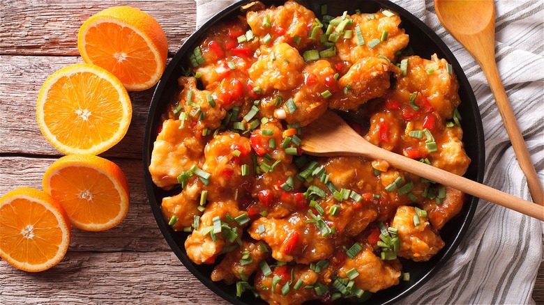 Orange chicken topped with chopped green onions in a black skillet with a wooden spoon