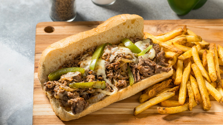 Grilled steak sandwich with onions and cheese on bun with french fries.