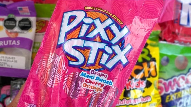 Hand holding a bright pink bag of Pixy Stix candy straws