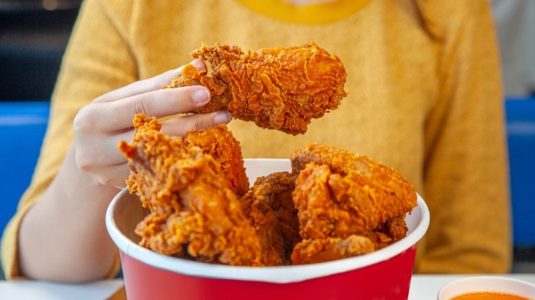 A person eating from a bucket of fried chicken.