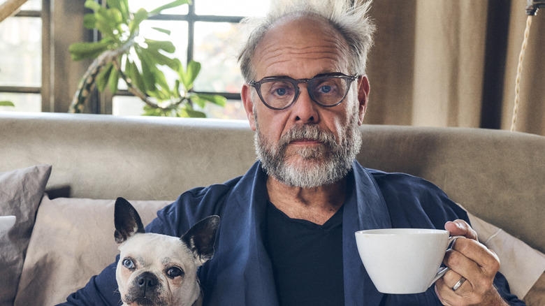 Alton Brown holds a coffee cup along with a dog.