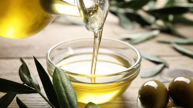 Pouring olive oil from a glass bottle into a small dish