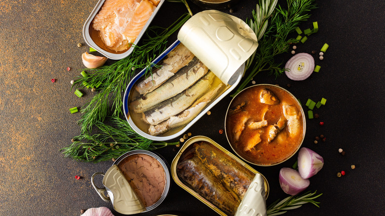 Various tinned fish, surrounded by fresh herbs like dill and some cut shallots.