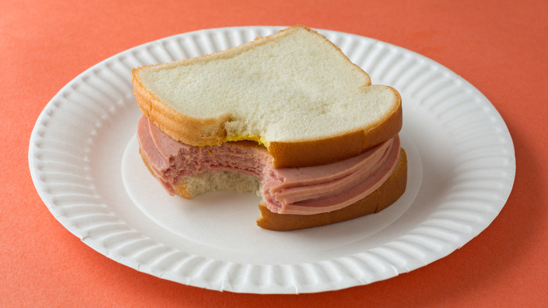 A bologna sandwich on white bread on a white paper plate.