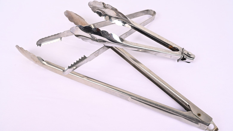 Stainless steel food tongs stacked on a white background.