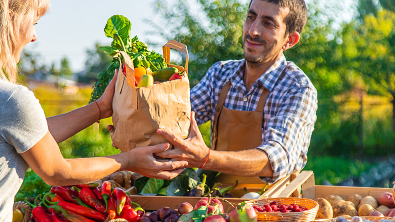 A vendor at a farmers market stand hands out a bag of produce to a customer.