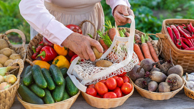 A woman places produce into a mesh fabric bag at a farmers market.