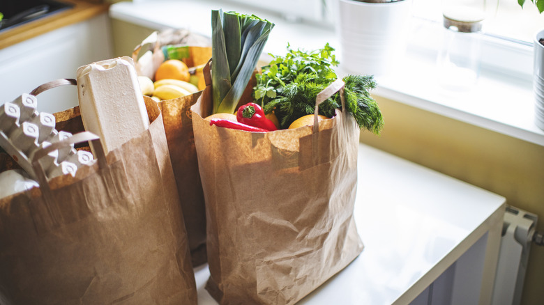 fresh groceries consisting of vegetables in three brown bags on counter
