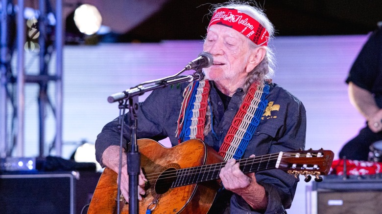 Willie Nelson performing with a guitar onstage.