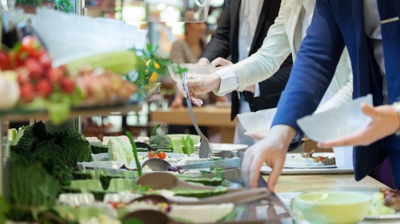 People helping themselves to salad at a salad bar.