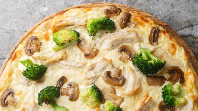 Cream pizza with chicken breast, broccoli and mushrooms close-up on wooden board on table.