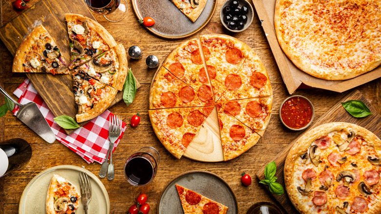 Flat-lay of different types of pizza and red wine on a wooden table.